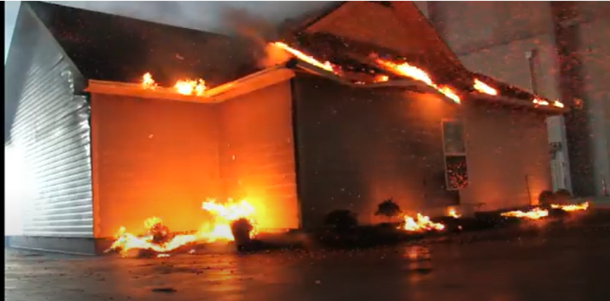 Screen shot of burning house demo by the IBHS- mulch and plants next to house, leaves in the gutters and on roof catch the house on fire